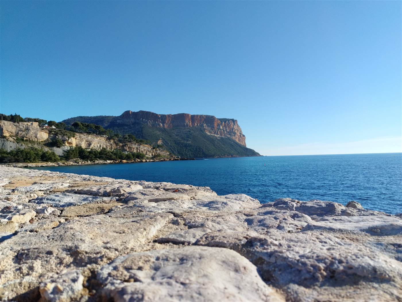 The bay at Cassis from the stone jetty, with the Cap Canaille cliffs rising behind deep-blue water under a clear sky